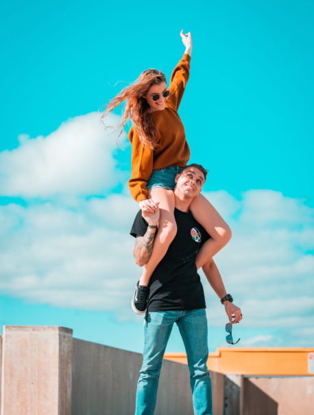 Girl riding shoulders of Man against a blue sky